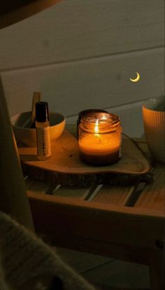 a lit candle sitting on top of a wooden table next to bowls and candles in front of a window