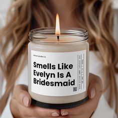 a woman holding a candle that says smells like evelyn is a bridesmaid on it