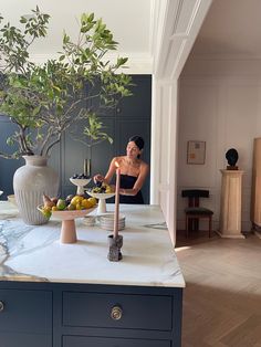 a woman standing in front of a table filled with fruit and plants on top of it