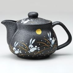 a black tea pot with white rabbits painted on it