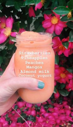 a hand holding up a jar of orange liquid with the words strawberries, pineapples, mangos, almond milk and coconut yogurt