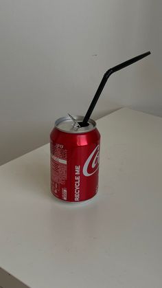 a soda can with a black straw sticking out of it's side on a white surface