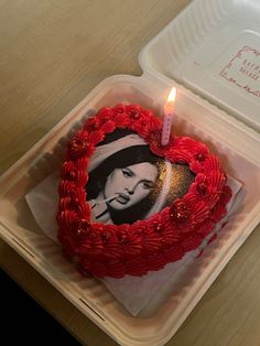 a heart shaped cake sitting on top of a plastic container with a candle in it