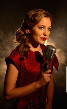 a woman in a red dress holding a microphone and looking at the camera with an intense look on her face