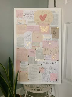 a white frame with pink and gold paper on it next to a potted plant