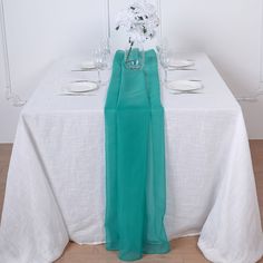 the table is set with white plates, silverware and green cloth draped over it