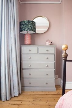 a bedroom with pink walls and a white chest of drawers in front of a mirror