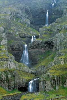 the waterfall is surrounded by green grass and tall rocks with water cascading from them