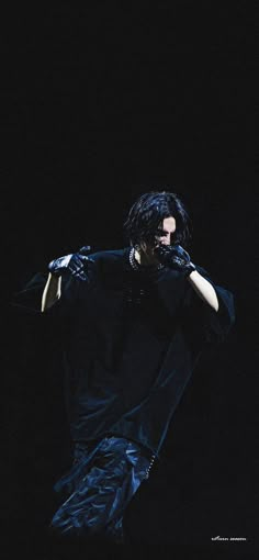 a man with long black hair and gloves on his face is performing in the dark