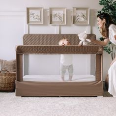 a woman holding a stuffed animal next to a baby in a crib on the floor