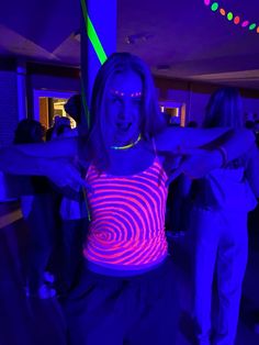 a woman is dancing in the dark with neon lights on her chest and hands behind her back