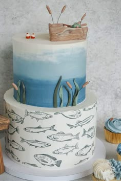 a three tiered cake with blue and white frosting, fish on the bottom