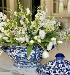 a blue and white vase filled with flowers on top of a marble counter next to a ceramic jar