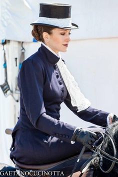 a woman riding on the back of a black horse wearing a top hat and gloves