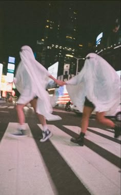 two people walking across a crosswalk in the city at night with long veils on their heads