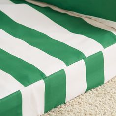 a green and white striped bed spread laying on top of a carpeted floor next to a pillow