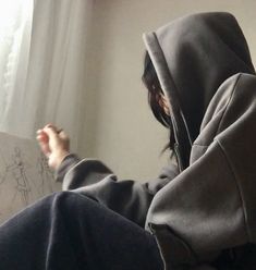 a person sitting in front of a window wearing a hoodie