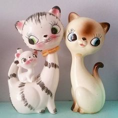 three ceramic figurines of cats sitting next to each other on a blue surface