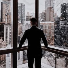 a man standing in front of a window looking out at the cityscape and skyscrapers