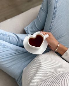 a person sitting on a couch holding a heart shaped coffee mug