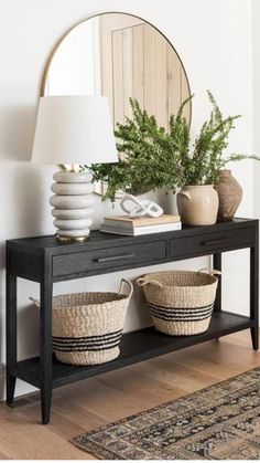 a black console table with two baskets and a round mirror on the wall behind it