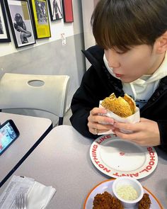 a young boy is eating some food at a table with his cell phone in front of him