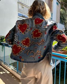 a woman wearing a jean jacket with hearts painted on it and standing next to a railing