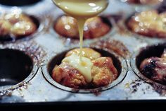 a person pouring sauce on some cupcakes in a muffin tin filled with them