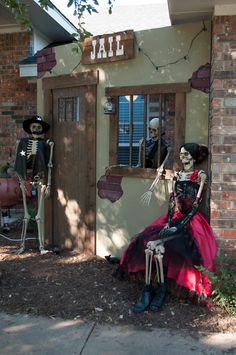 two skeletons dressed up in costumes sitting on the ground next to a building with a sign that says jail