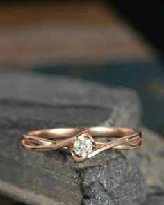 a rose gold engagement ring with a diamond in the center on top of a rock