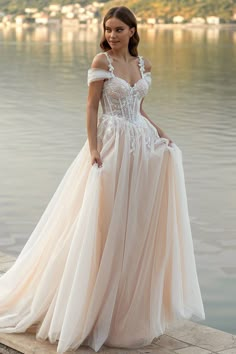 a woman in a wedding dress standing by the water