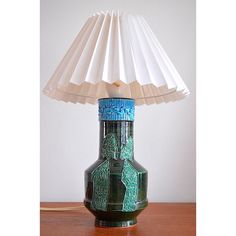 a green vase with a white paper shade on it sitting on top of a wooden table