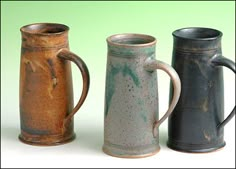 three different colored mugs sitting next to each other on a white surface with green background