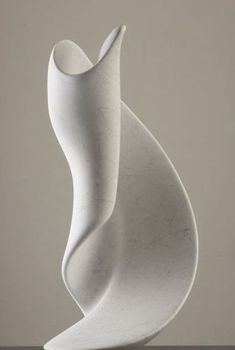 a white sculpture sitting on top of a wooden table next to a gray wall and floor