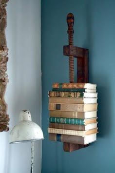 a stack of books sitting on top of a wooden shelf next to a wall mounted light