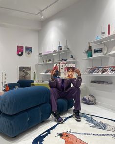 a man sitting on a blue couch reading a magazine in a room filled with furniture