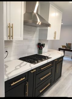 a kitchen with black cabinets and white marble counter tops, gold trimmings on the backsplash