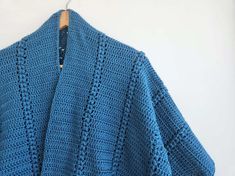 a blue crocheted sweater hanging on a wooden hanger next to a white wall