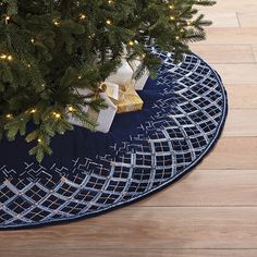 a christmas tree with presents under it on a blue round rug next to a pine tree