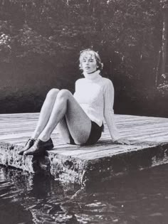 a woman is sitting on a dock by the water