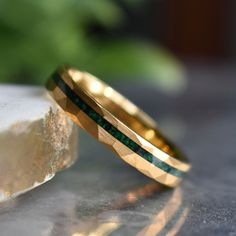 two gold wedding bands with green and black stones on top of each other in front of a rock