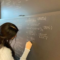 a woman writing on a blackboard with white chalk