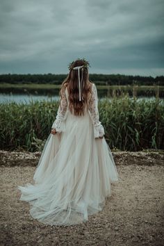 a woman in a wedding dress standing by the water wearing a flower crown on her head