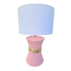 a pink table lamp with a white shade on the top and gold trim around the base