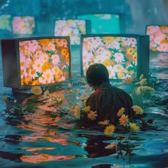 a man sitting in the water next to four televisions with flowers on them and one person watching