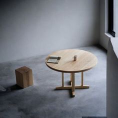 a round wooden table sitting in front of a window next to a block of wood