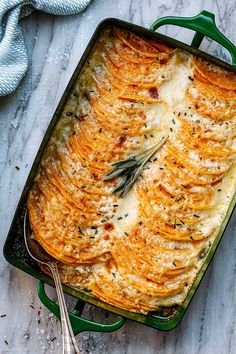 a green casserole dish with potatoes and herbs on top, next to a spoon