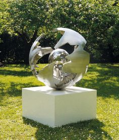 a metal sculpture sitting on top of a white block in the grass next to trees