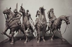 four statues of men riding horses and holding spears on a shelf in front of a wall