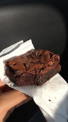 a hand holding a piece of chocolate brownie on top of a white paper towel